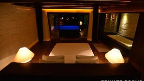A private room with a bed, a small table, and two lamps. There is a view of a pool and a night scene outside. - Manaspark Deluxe Hotel (Fethiye)