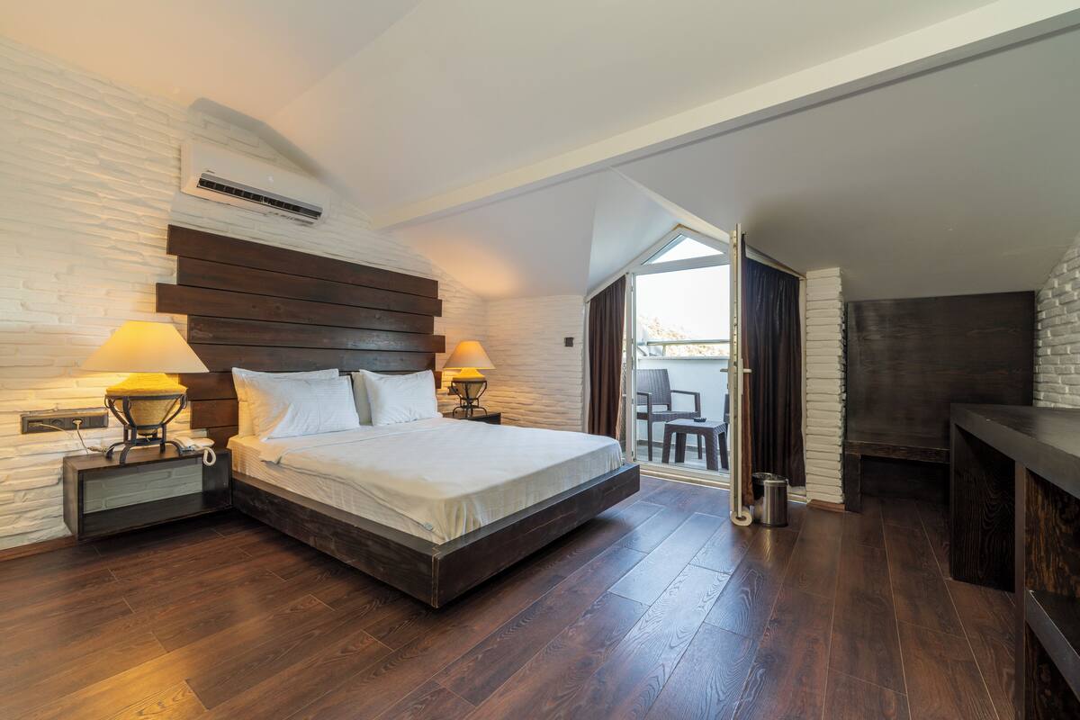 A modern bedroom with a large bed, wooden headboard, two bedside lamps, and a view of the outdoors through a sliding door.