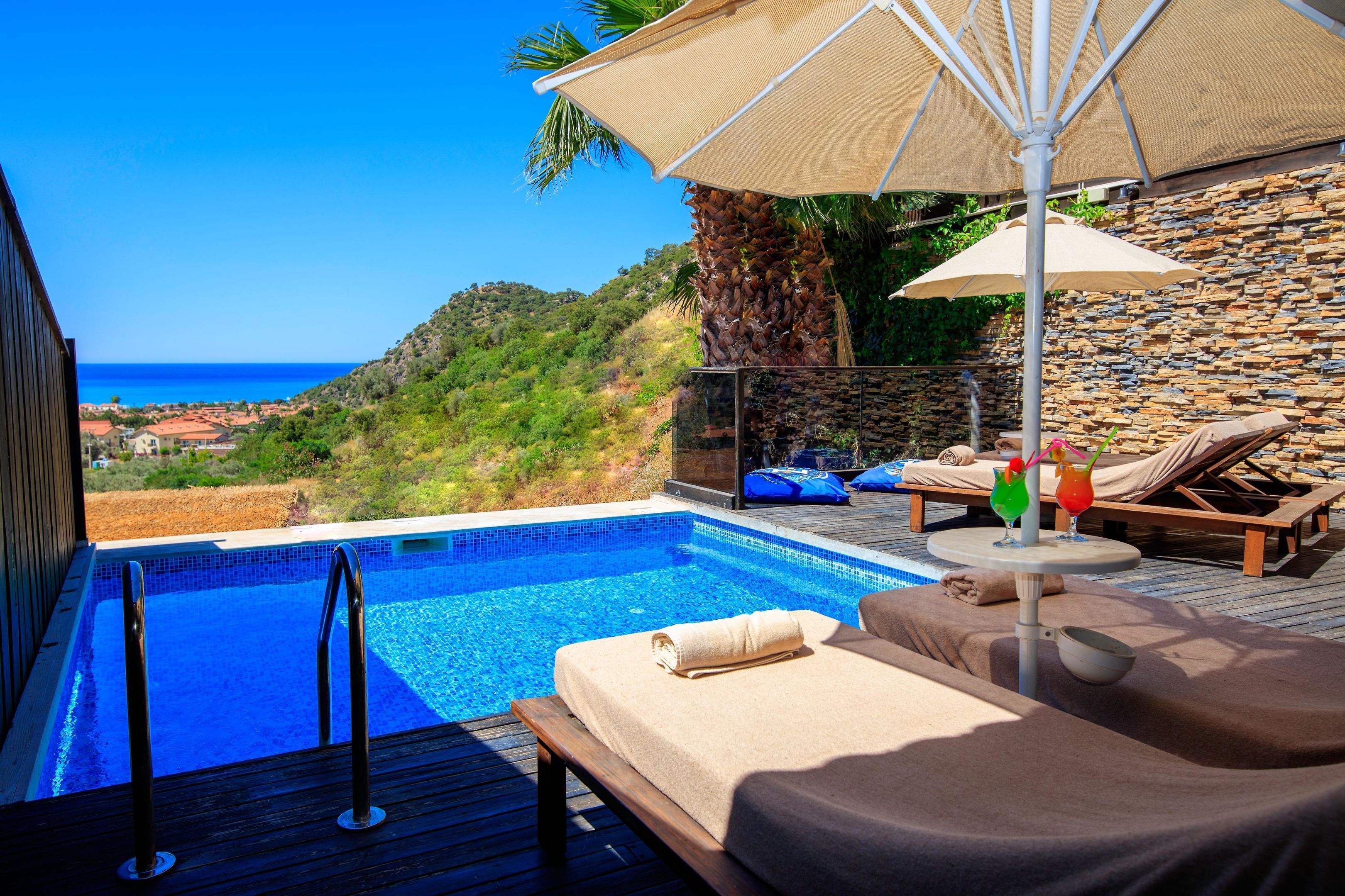 A poolside area with a view of the sea, lounge chairs, and a stone wall.