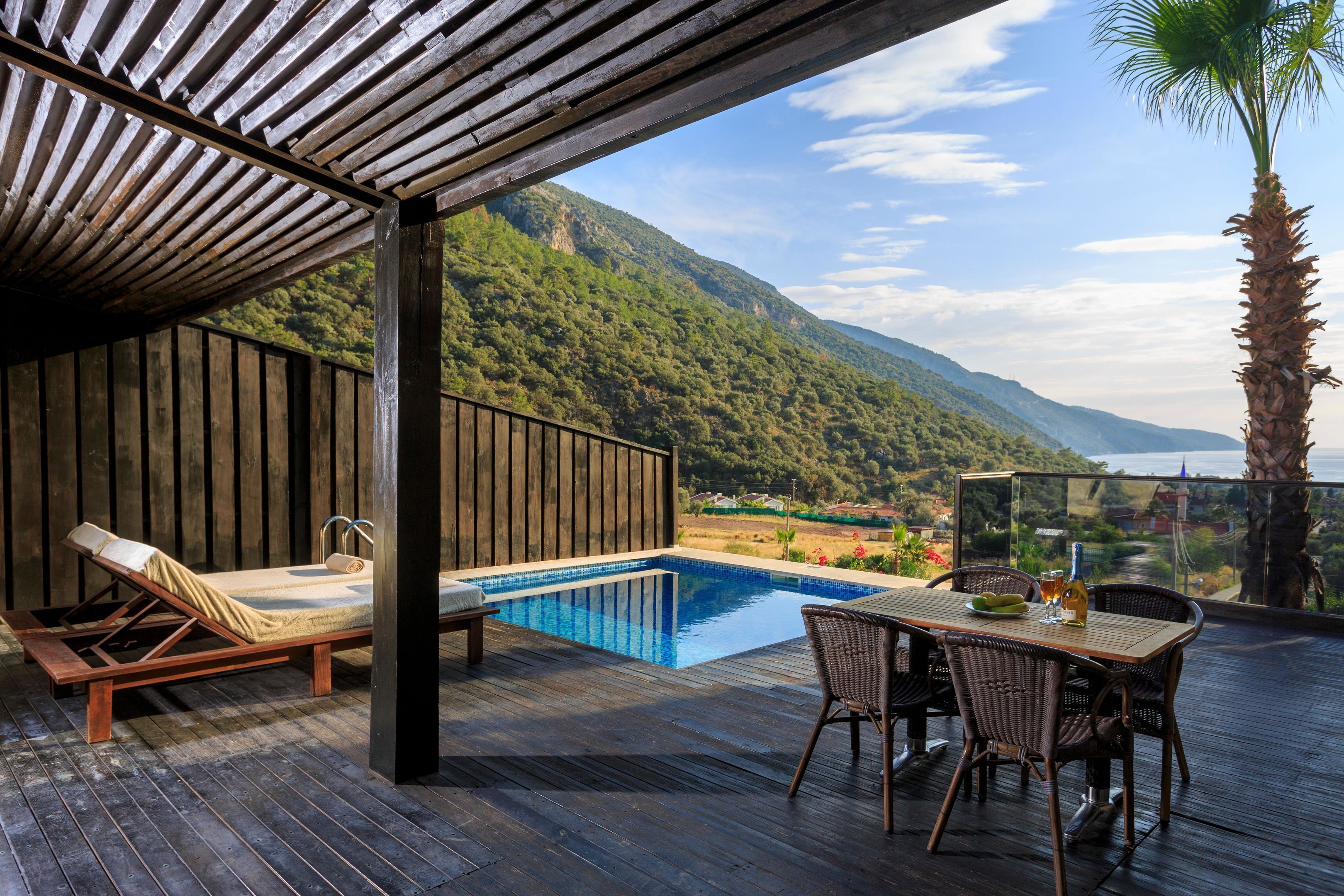 Une terrasse en bois avec une piscine, des chaises longues et une table avec des chaises.