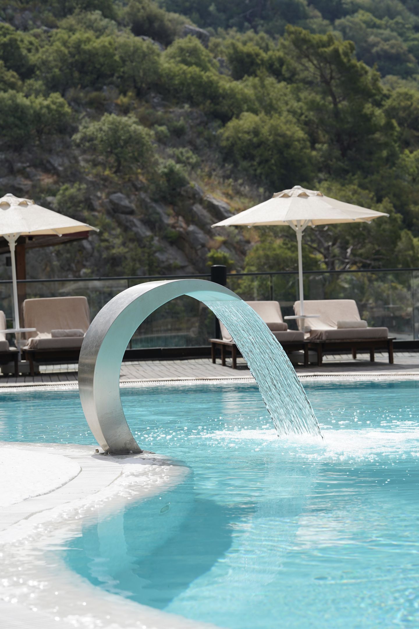 A pool with a modern water feature, lounge chairs, and umbrellas.