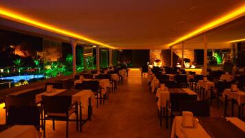 A restaurant with a long table layout, large windows, and a view of a water feature outside.