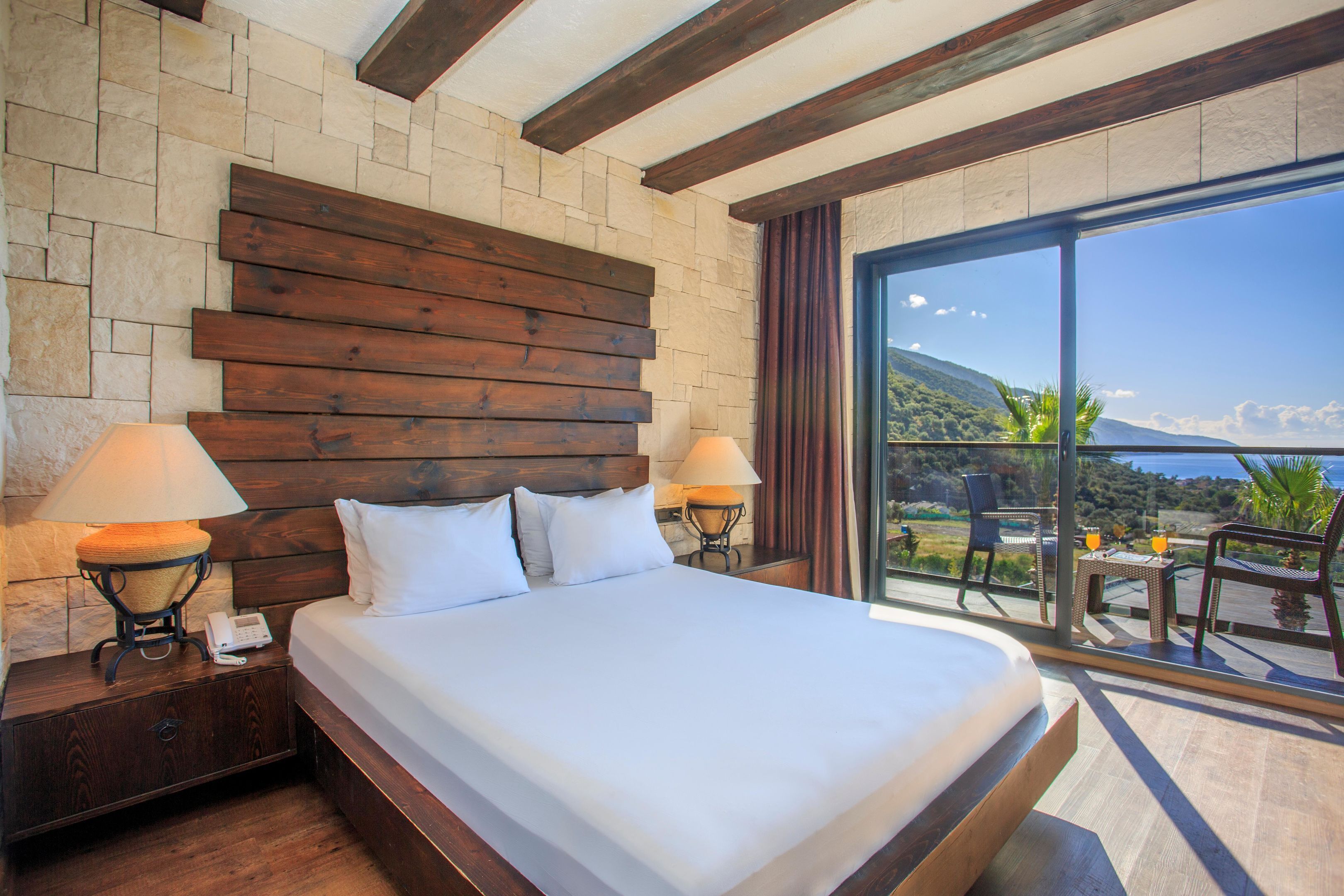 Ein Hotelzimmer mit einem großen Bett, einem Holz-Kopfteil, zwei Nachttischlampen, einem Nachttisch und Blick ins Freie.