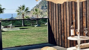 A terrace with a wooden railing, a table with wine glasses and a bottle, and a view of the sea and hills. - Manaspark Deluxe Hotel (Fethiye)