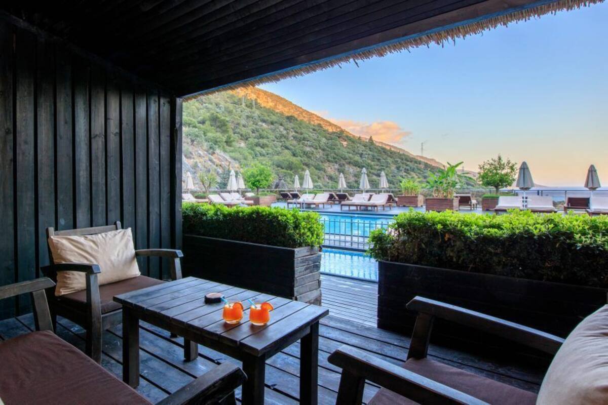 A wooden deck with a table and chairs, overlooking a pool and lounge area with umbrellas.