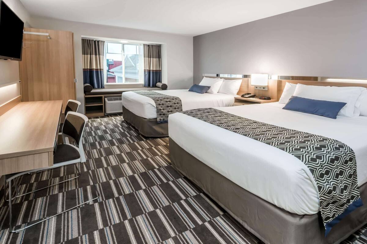 Ein Hotelzimmer mit zwei Betten, einem Schreibtisch, einem Sessel, einem Fernseher und einem Fenster mit Vorhängen.