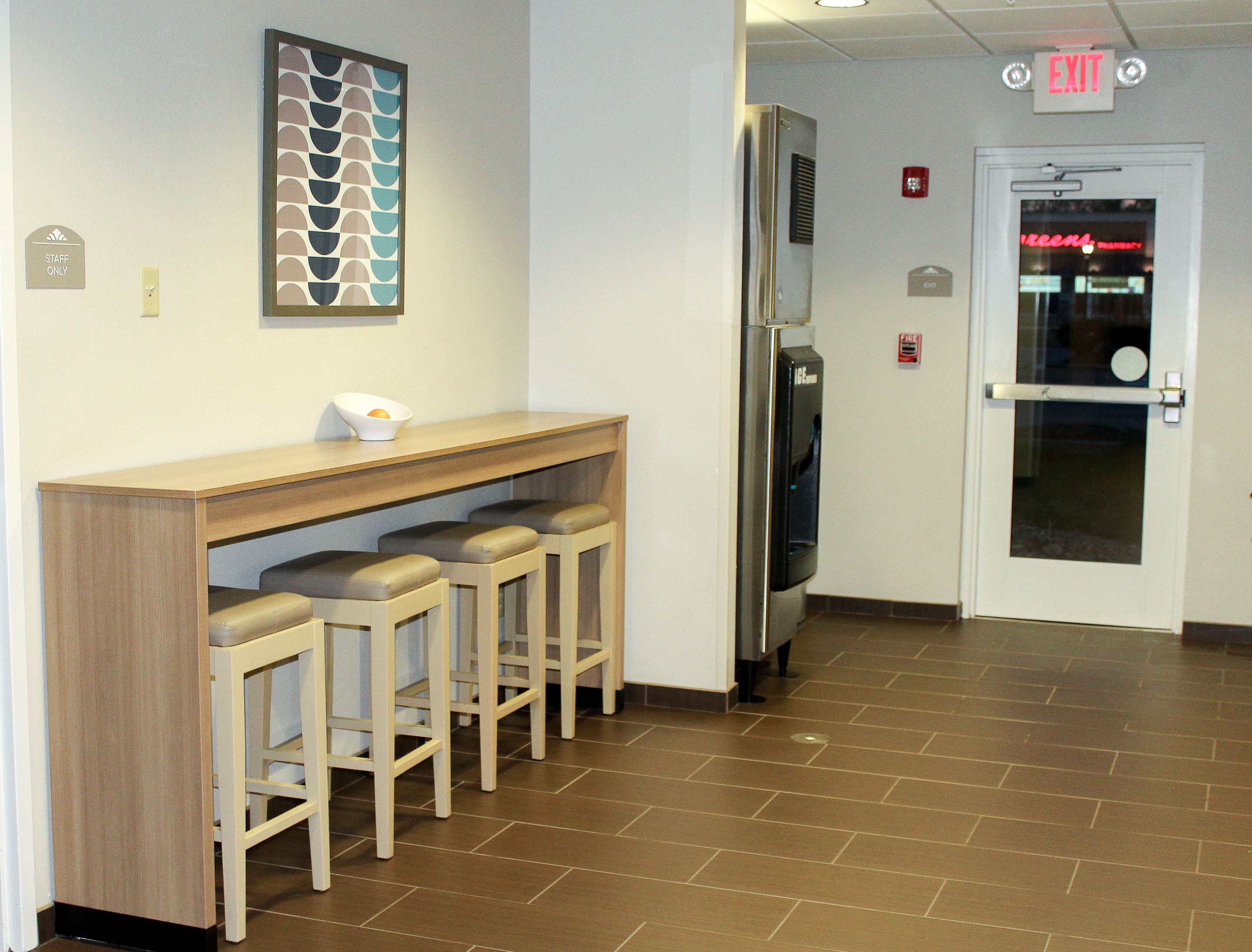 A hallway with a bar area featuring a counter and stools, a refrigerator, and an exit door with a neon sign.