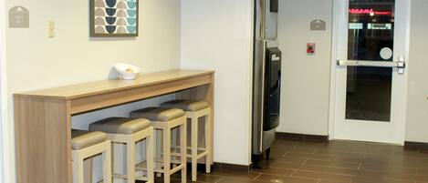 Corredor com área de bar, incluindo balcão e banquetas, geladeira e porta de saída com letreiro neon.