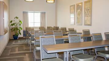 Une salle de conférence équipée de plusieurs tables et chaises, d’une plante en pot et de trois luminaires fixés au mur.