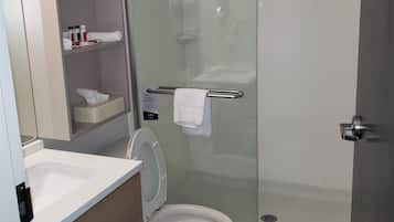 A modern bathroom with a glass-enclosed shower, a white toilet, a sink with a mirror, and a shelf with toiletries.
