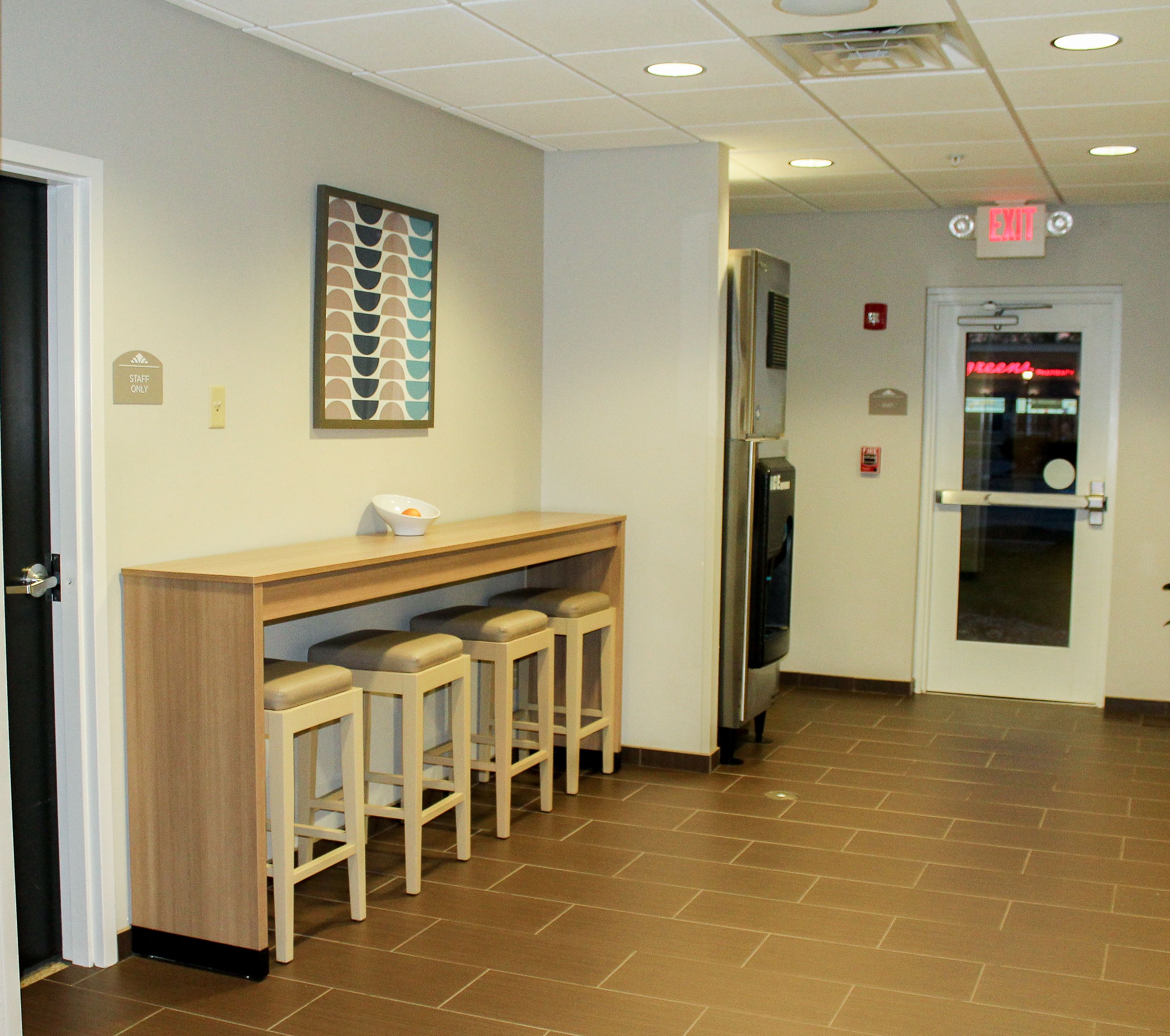 A hallway with a bar area, stools, a refrigerator, and an exit sign.