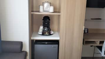 Una kitchenette compacta con cafetera, un refrigerador pequeño y un microondas en un estante.