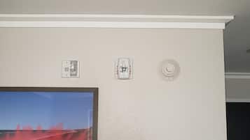 Un muro con tre termostati, un rilevatore di fumo e un quadro incorniciato.