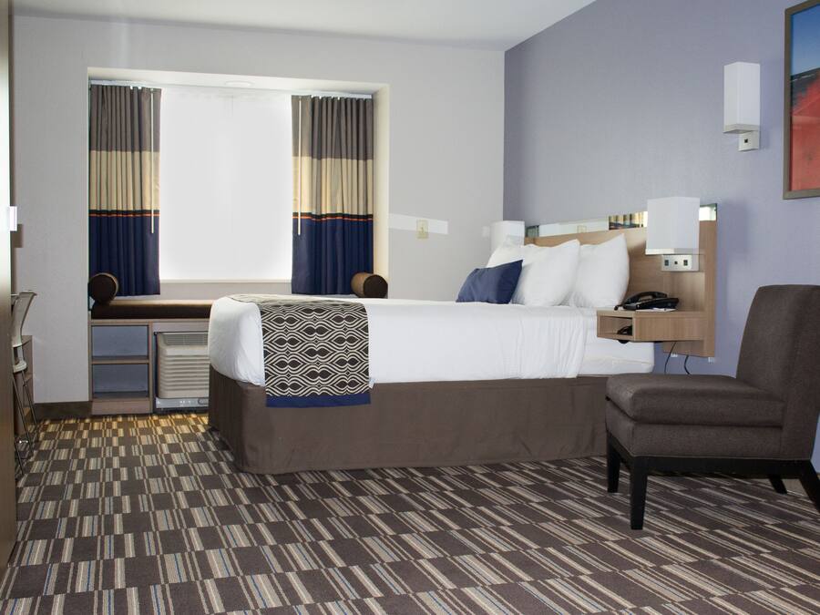 A hotel room with a bed, a desk, a chair, a nightstand, and a window with curtains.
