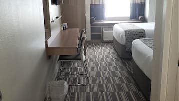 A hotel room with a bed, a desk, a chair, a small table, a mirror, and a window with curtains.