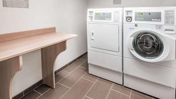 A laundry room with two white Bosch washing machines, a wooden bench, and a tiled floor.