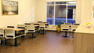 A conference room with white tables and chairs, a large window with a view of a parking lot, and a painting on the wall.