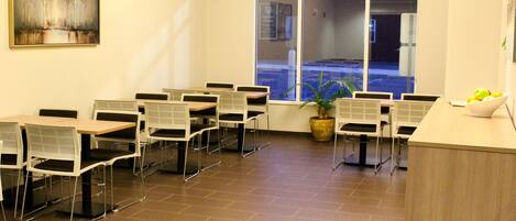 A conference room with white tables and chairs, a large window with a view of a parking lot, and a painting on the wall.