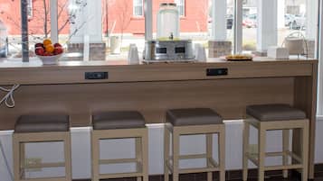 A kitchen counter with a fruit bowl, a water dispenser, and a plate of food. There are three stools in front of the counter.