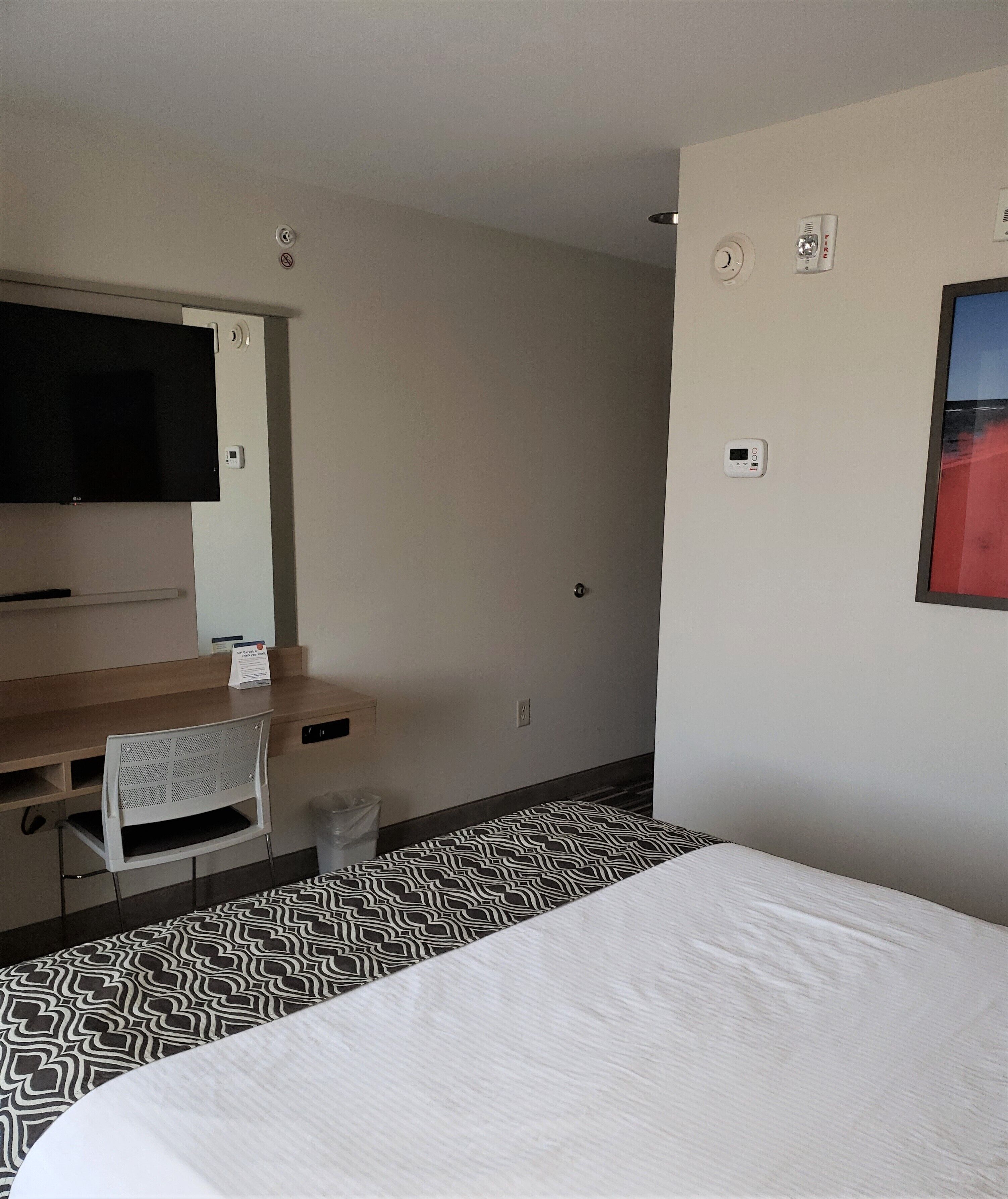 Ein Hotelzimmer mit einem Bett, einem Schreibtisch, einem Sessel, einem Fernseher und einem Rauchmelder.