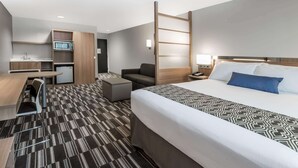 A hotel room with a bed, a desk with a chair, a sofa, a small kitchenette, and a bathroom. - Microtel by Wyndham Penn Yan Finger Lakes Region (Penn Yan)