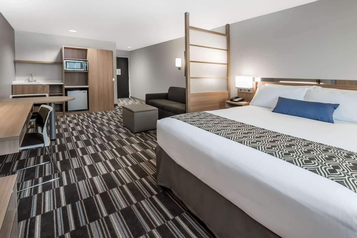 Ein Hotelzimmer mit Bett, Schreibtisch mit Stuhl, einer Sitzecke und einer kleinen Küche sowie einem Badezimmer.