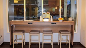 A bar area with a large window, three stools, and a bowl of fruit. - Microtel by Wyndham Penn Yan Finger Lakes Region (Penn Yan)