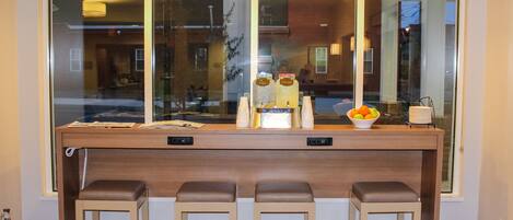 A bar area with a large window, three stools, and a bowl of fruit.
