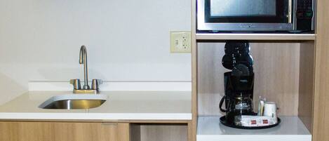 A compact kitchenette with a sink, microwave, coffee maker, and a small refrigerator.