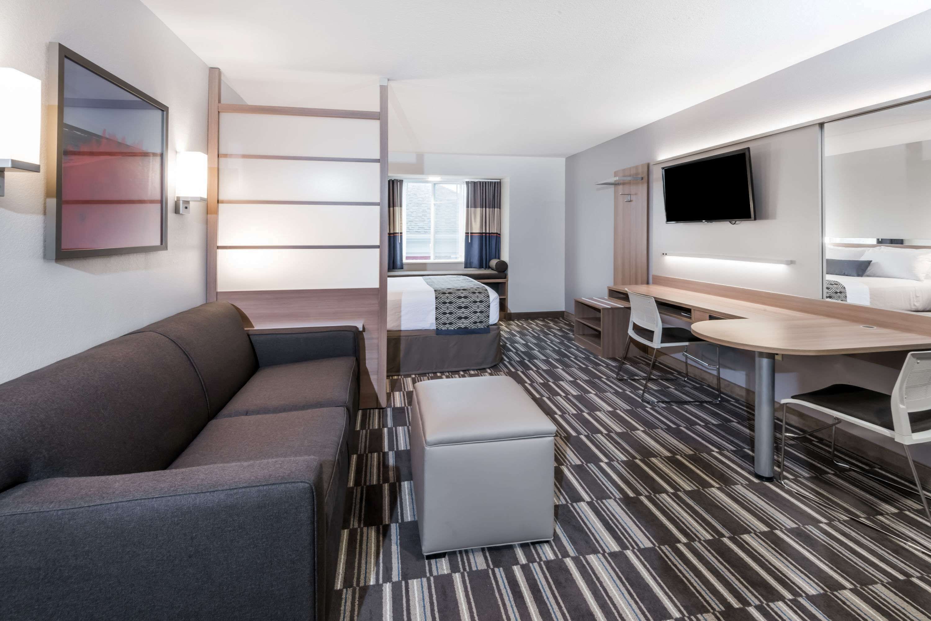 Una habitación de hotel moderna con sofá, una mesita, televisor y cama con cortinas.