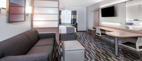 Una habitación de hotel moderna con sofá, una mesita, televisor y cama con cortinas.