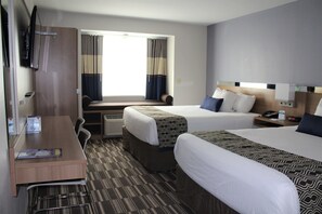 A hotel room with two beds, a desk, a television, and a window with curtains. - Microtel by Wyndham Penn Yan Finger Lakes Region (Penn Yan)