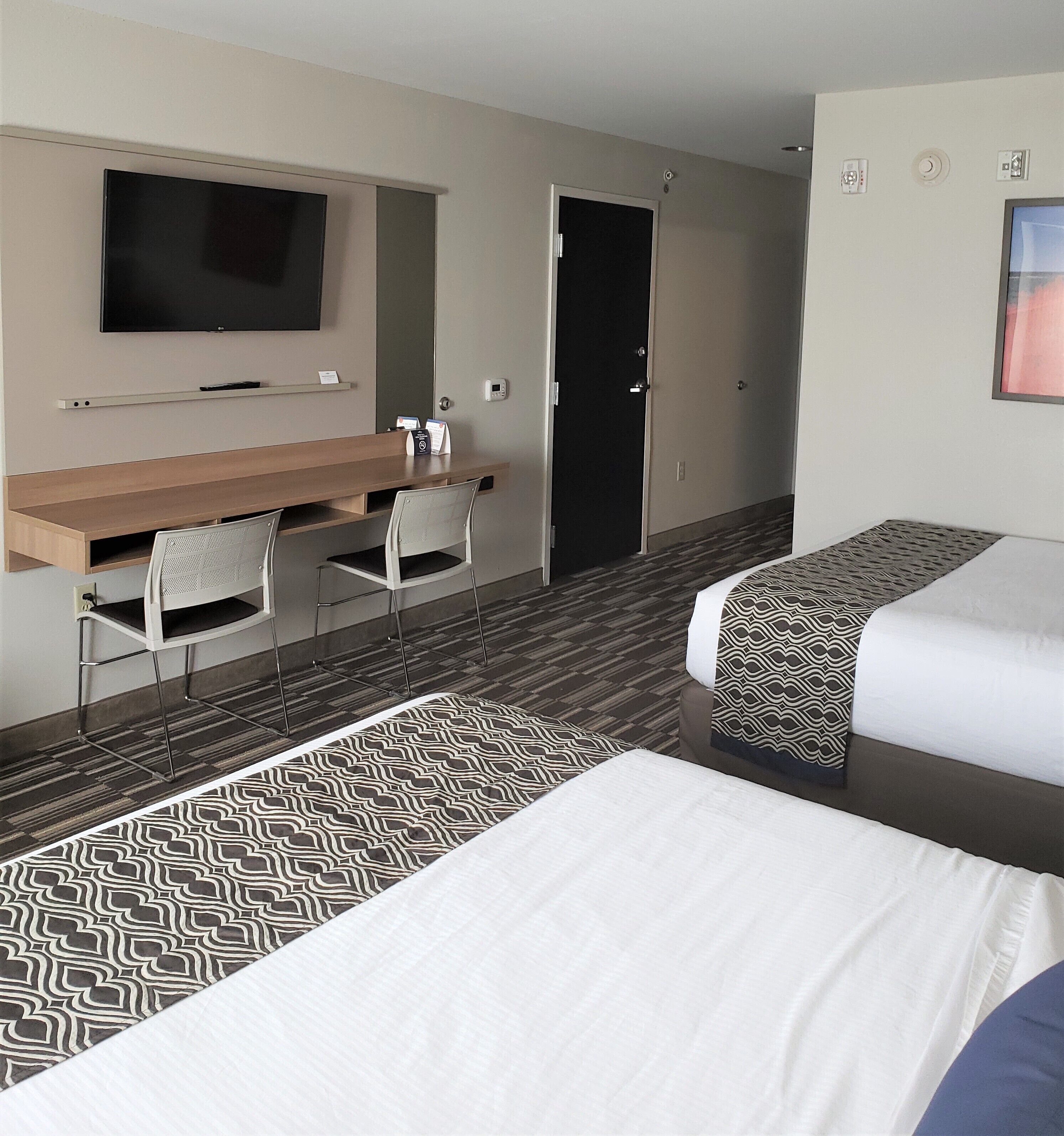A hotel room with a desk, two beds, a TV, and a door.