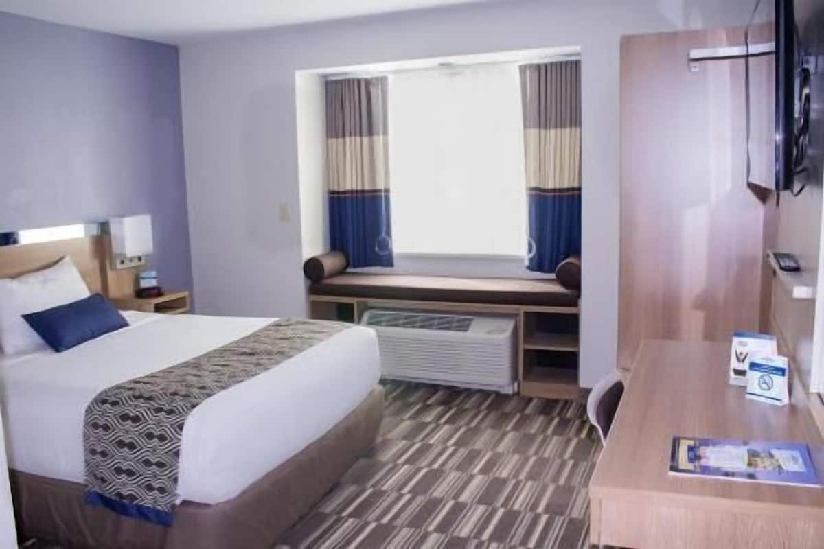 Ein Hotelzimmer mit Bett, Schreibtisch, Fenster mit Vorhängen und Fernseher.