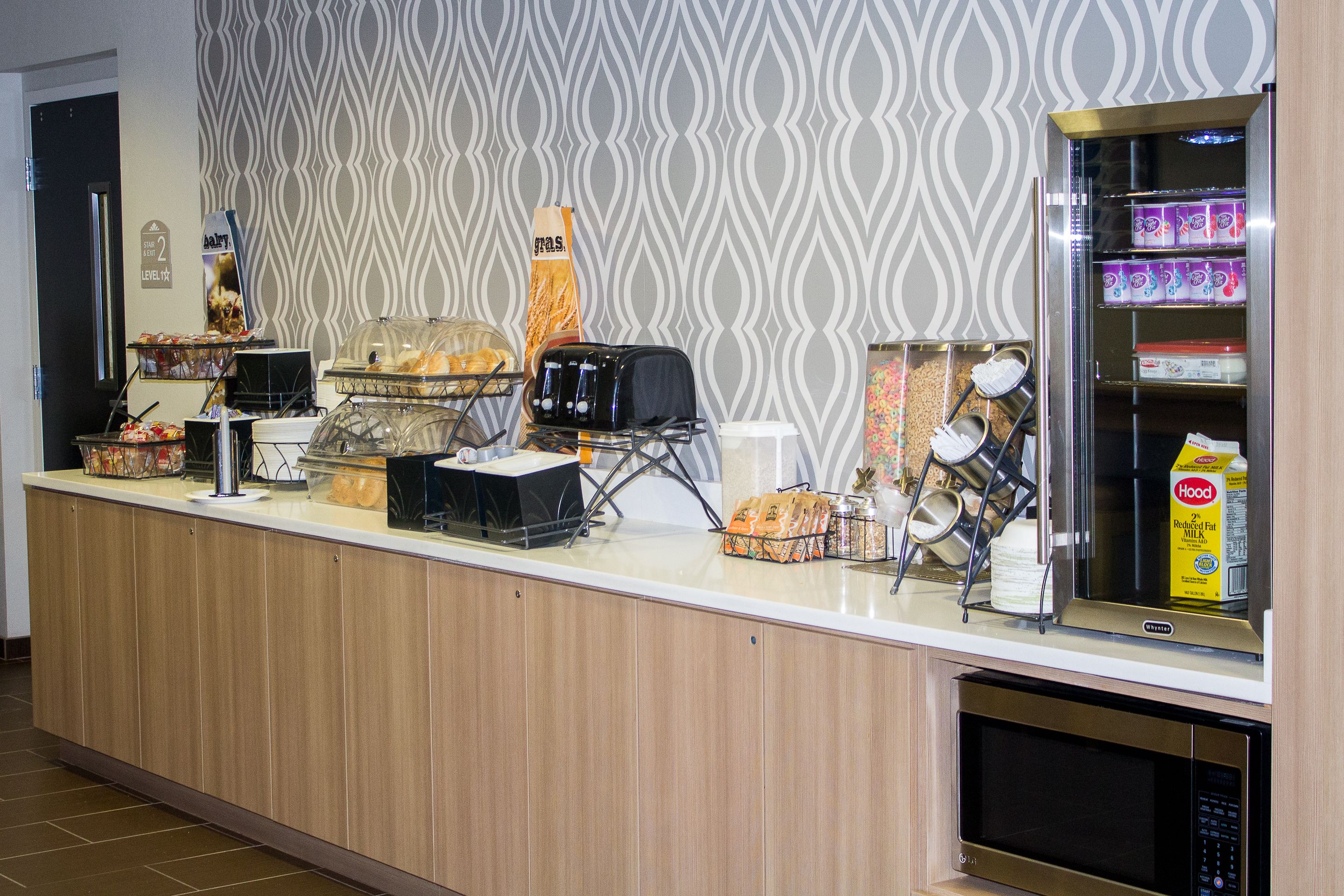 A hotel reception area with a counter, a coffee machine, a microwave, and a refrigerator stocked with beverages.