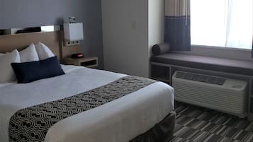 Une chambre d’hôtel comprenant un lit, une table de chevet, une fenêtre avec des rideaux et un système de climatisation intégré.