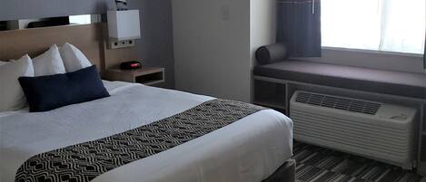 Ein Hotelzimmer mit Bett, Nachttisch, Fenster mit Vorhängen und einer eingebauten Klimaanlage.