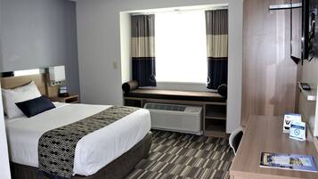 A hotel room with a large bed, a desk, a chair, a window with curtains, a radiator, and a television.