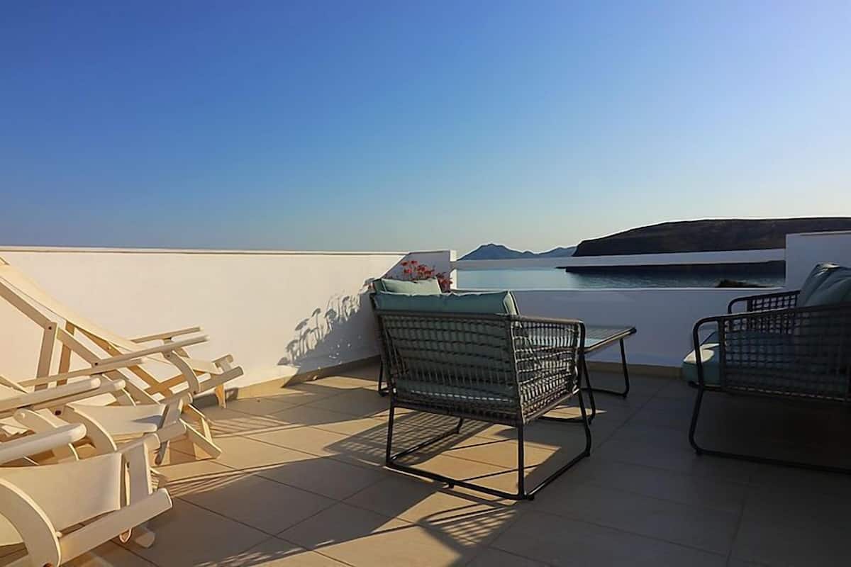A terrace with chairs and a table overlooking a body of water and distant land.