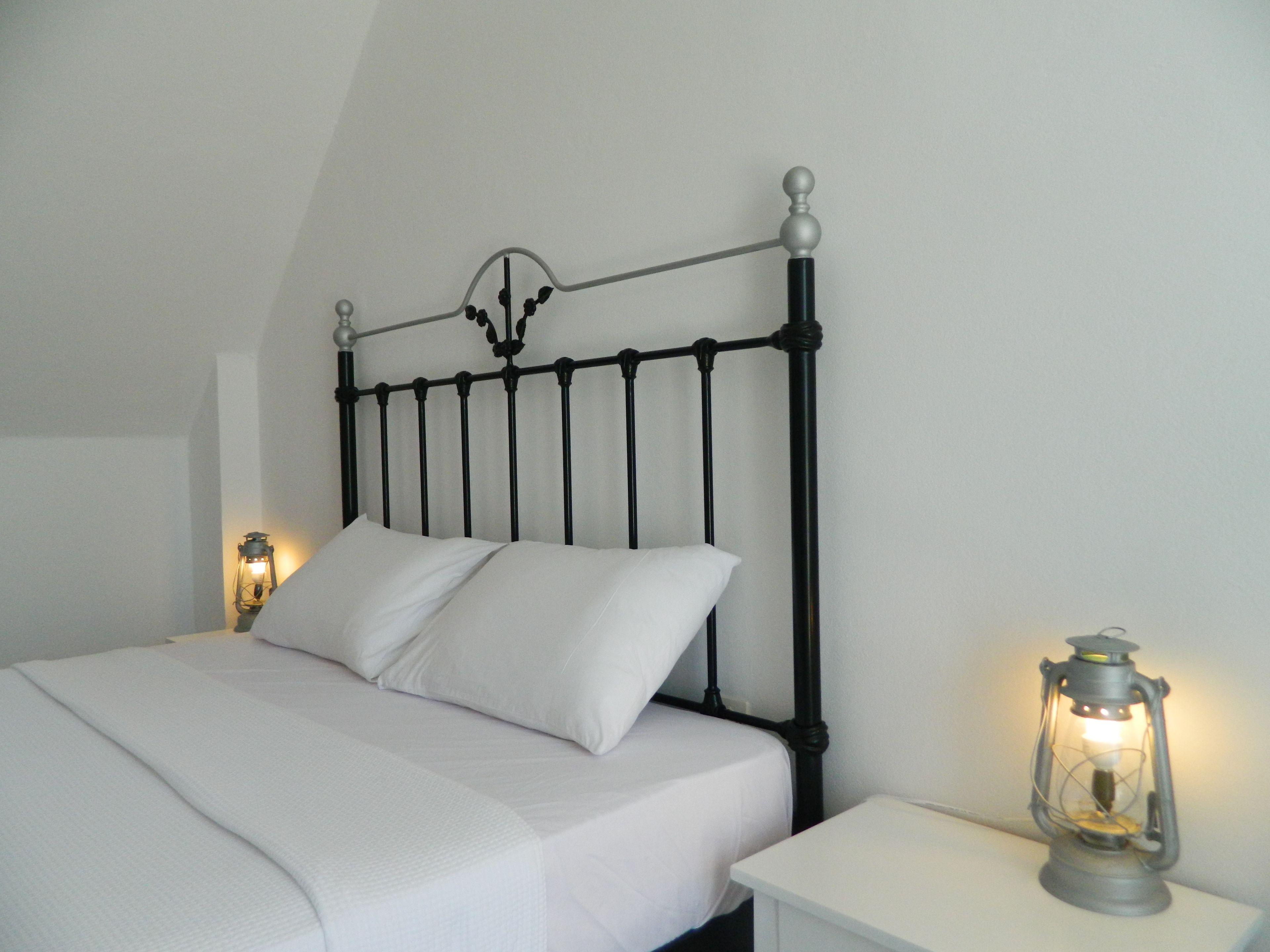 A bed with a black metal headboard, white bedding, and two bedside tables with lantern-style lamps.