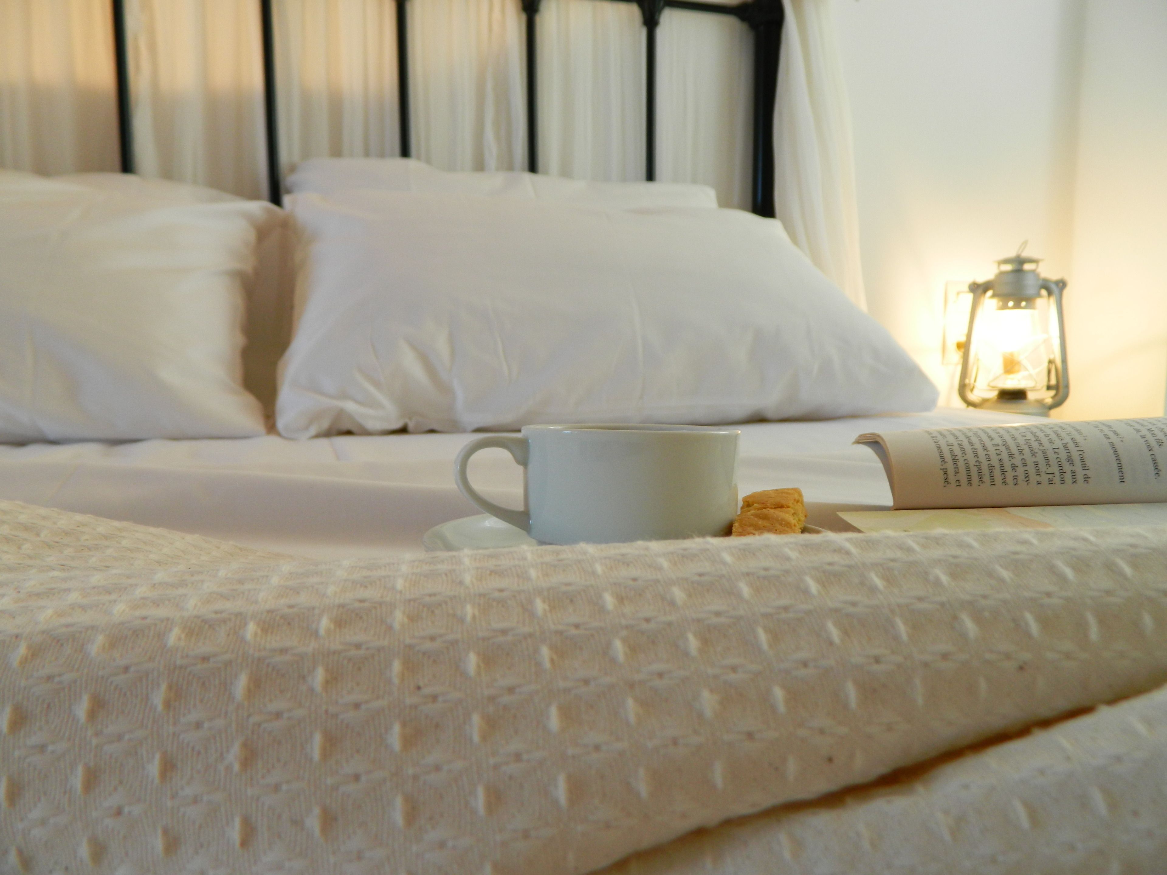 Ein ordentlich bezogenes Bett mit weißen Leinen, eine weiße Tasse, ein Keks und ein Buch auf einem Nachttisch.