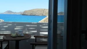 A balcony with a table and chairs, overlooking a coastal landscape with clear blue sea and distant hills. - Avra Pahainas Hotel (Milos)