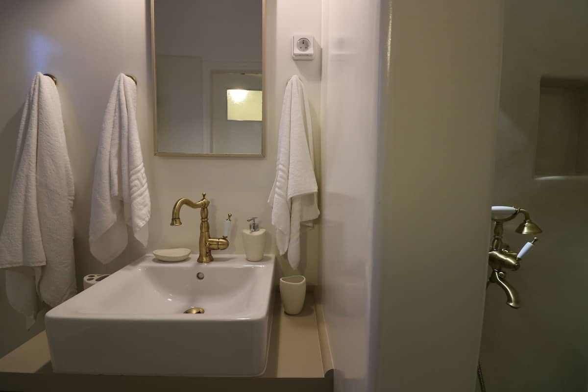 A bathroom with a white sink, gold faucets, a mirror, and two towels hanging on hooks.
