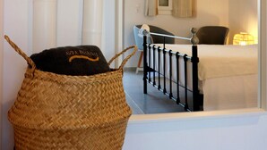 A room with a bed, a bedside table, a lamp, and a woven basket on a chair. - Avra Pahainas Hotel (Milos)