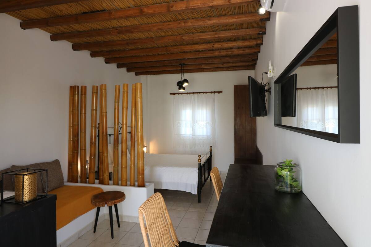 A room with a bed, a sofa, a dining table, and a TV mounted on the wall.