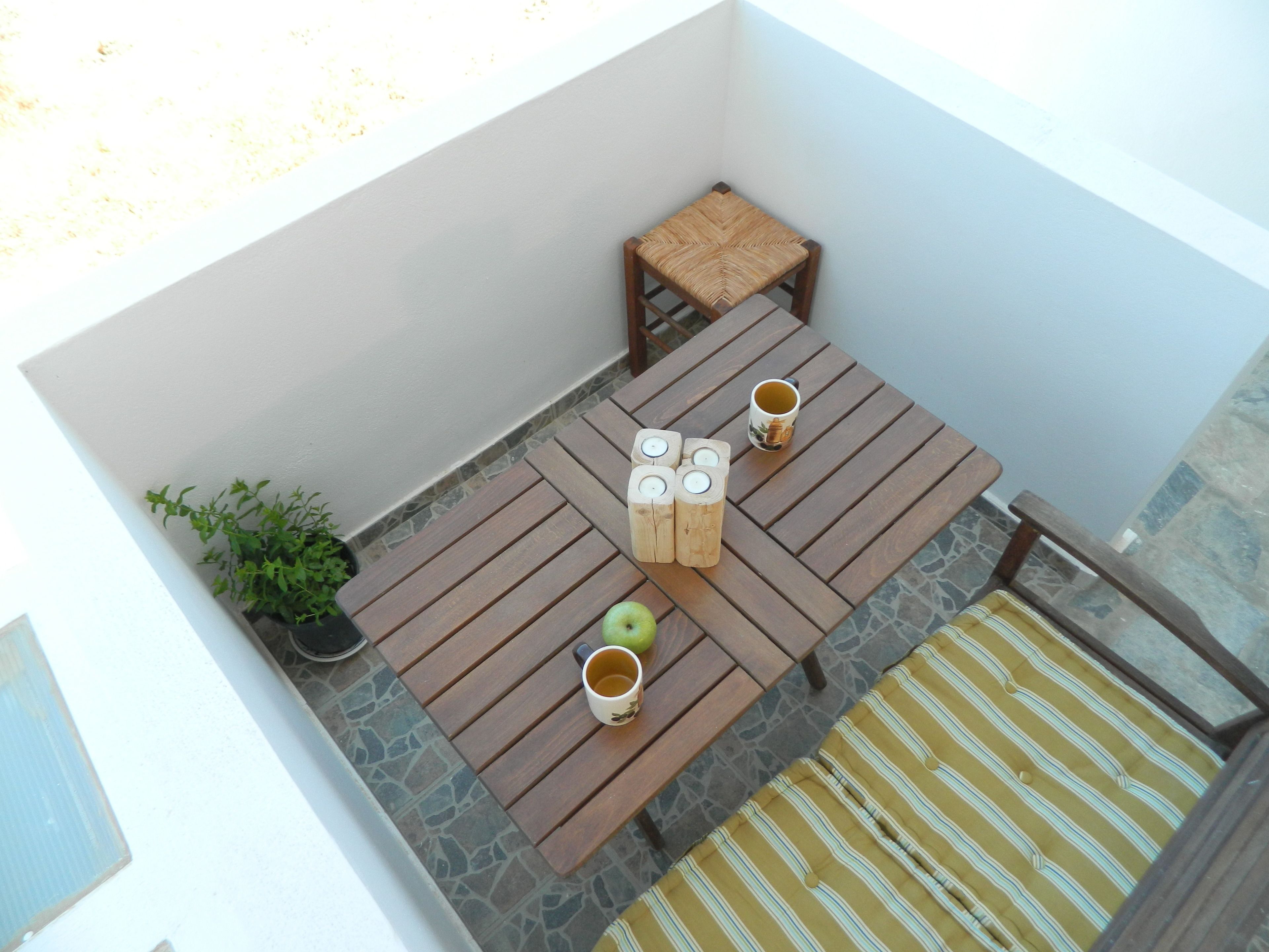 A small outdoor patio with a wooden table and chairs, a potted plant, and a striped cushion.
