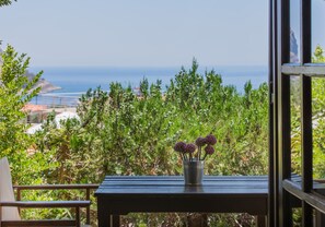 Un balcón con una mesa metálica y una silla, con vistas a un jardín exuberante y al mar.