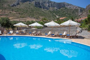 Zona de piscina con sillones reclinables y sombrillas, en un paisaje montañoso.