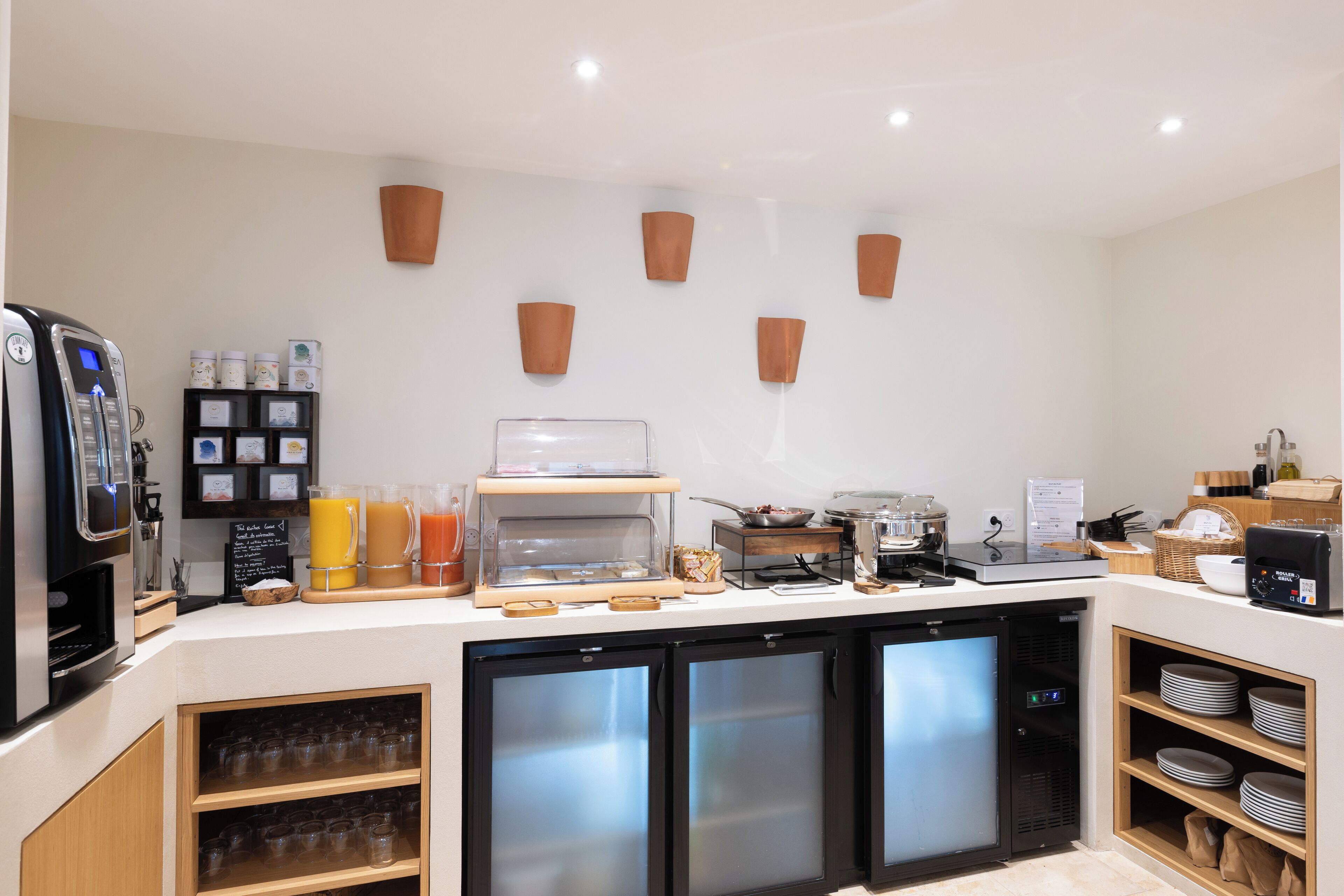 Un comptoir-bar moderne équipé d’une machine à café, d’un distributeur de jus et d’un présentoir réfrigéré.