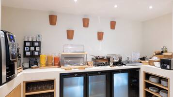 Un comptoir-bar moderne équipé d’une machine à café, d’un distributeur de jus et d’un présentoir réfrigéré.